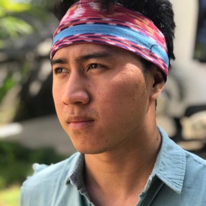 May include: A man wearing a blue shirt with a red, blue, and white patterned headband.