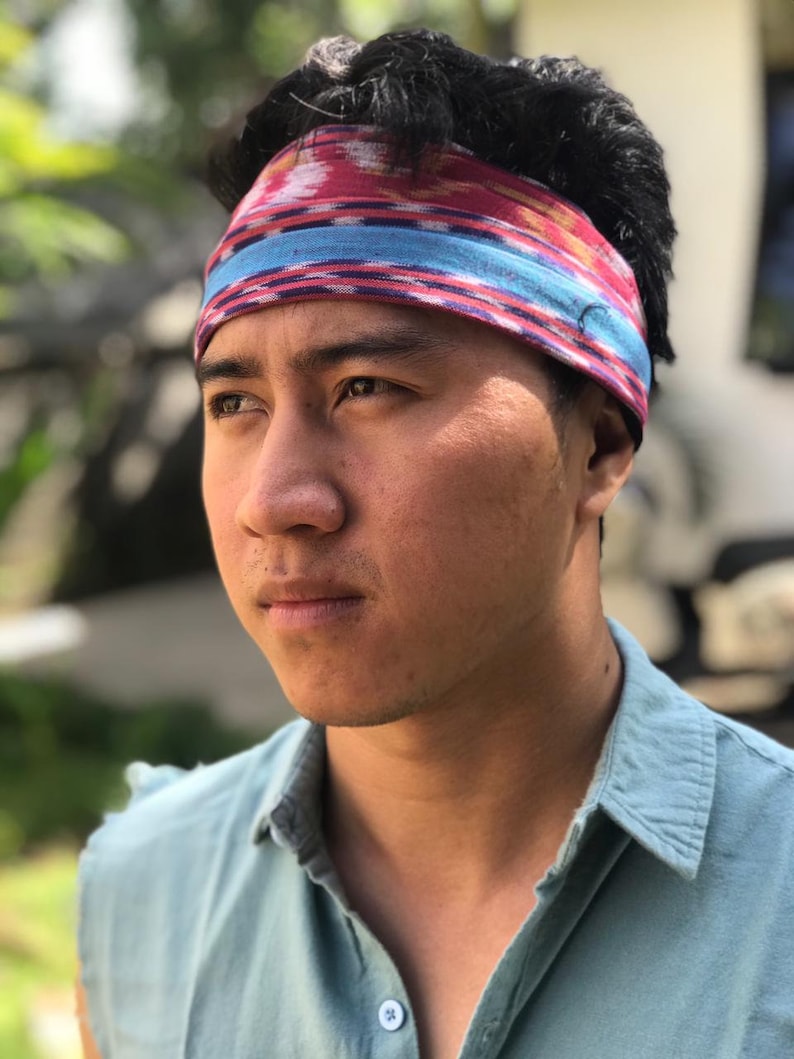 May include: A man wearing a blue shirt with a red, blue, and white patterned headband.