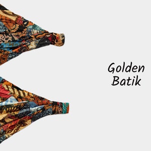 May include: Two colorful fabric headbands with a batik pattern in shades of blue, red, orange, and brown. The text "Golden Batik" is written in black below the headbands.