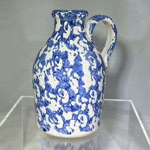May include: A small, white ceramic pitcher with a blue and white floral pattern. The pitcher has a handle and a spout.