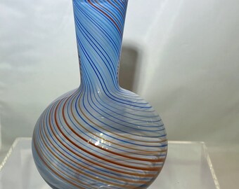 May include: A small, round glass vase with a narrow neck. The vase is decorated with swirling blue, white, and orange stripes.