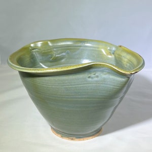 Puede incluir: Un tazón grande de cerámica verde con un borde ondulado. El tazón tiene un esmalte verde claro con un brillo sutil.