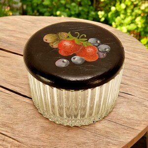 Può includere: Un barattolo di vetro con un coperchio nero che presenta un disegno dipinto a mano di fragole, mirtilli e ribes. Il barattolo ha un design a coste ed è perfetto per riporre piccoli oggetti.