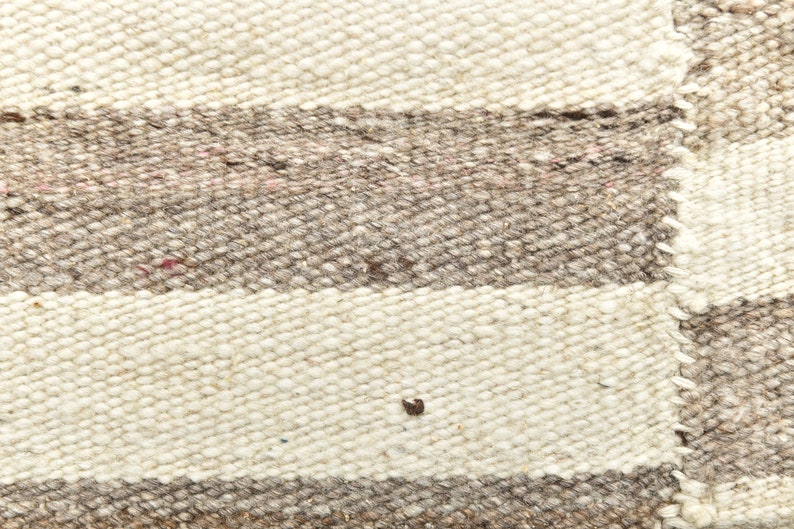 May include: Close-up of a woven rug with white and brown stripes. The rug is made of natural fibers and has a rough texture.