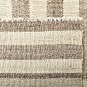 May include: A close-up of a woven rug with a striped pattern in shades of beige and brown. The rug has a fringed edge.