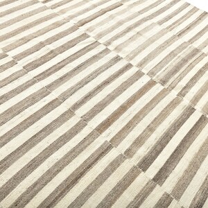 May include: A white and brown striped rug with a woven texture. The rug is made of natural fibers and has a simple, elegant design.
