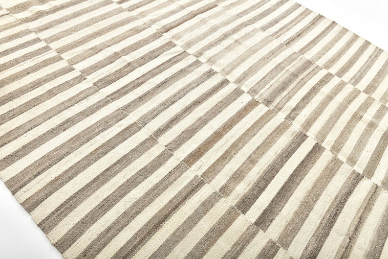 May include: A white and brown striped rug with a woven texture. The rug is made of natural fibers and has a simple, elegant design.