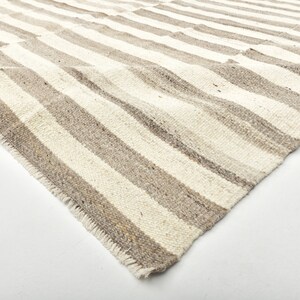 May include: A close-up of a white and gray striped rug with a frayed edge. The rug is folded in half and the texture of the fabric is visible.