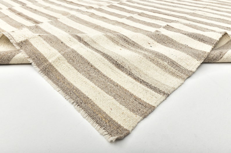 May include: A close-up of a white and gray striped rug with a frayed edge. The rug is folded in half and the texture of the fabric is visible.