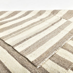 May include: A white and gray striped rug with a woven texture. The rug is folded in half, showing the underside of the rug.