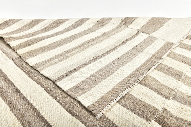 May include: A white and gray striped rug with a woven texture. The rug is folded in half, showing the underside of the rug.