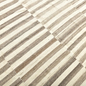 May include: A white and gray striped rug with a woven texture. The rug is made of natural fibers and has a rustic look.