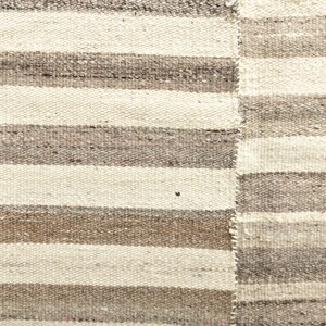 May include: A close-up of a woven rug with alternating stripes of white and brown. The rug has a rough, textured surface.