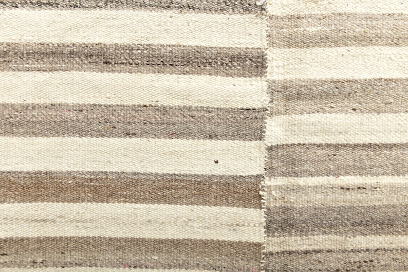 May include: A close-up of a woven rug with alternating stripes of white and brown. The rug has a rough, textured surface.