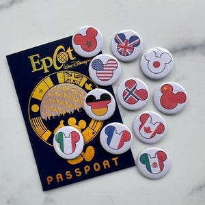 Puede incluir: Un folleto azul marino "Pasaporte" con letras doradas y un diseño dorado, rodeado de botones redondos blancos. Cada botón presenta un diseño de cabeza de Mickey Mouse con una bandera de diferentes países, incluidos EE. UU., Reino Unido y Alemania.