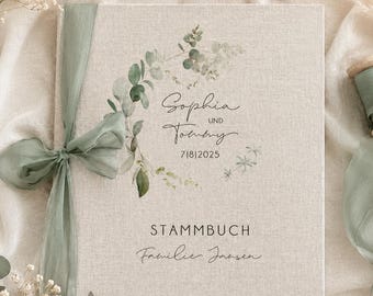 May include: A square beige linen-covered book with a sage green ribbon tied on the left side. The cover features a printed eucalyptus wreath, the names Sophia und Tommy, the date 7|8|2025, the word STAMMBUCH, and the text Familie Jansen.