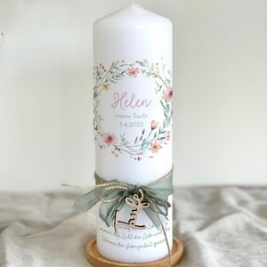 May include: A white pillar candle decorated with a floral wreath and the name "Helen". The candle is adorned with a green ribbon, a wooden charm, and rests on a wooden coaster. The text "meine Taufe 5.4.2025" is also visible.