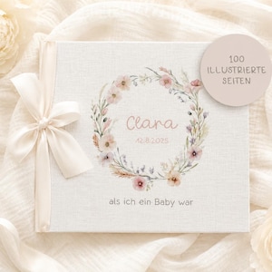Könnte beinhalten: Ein quadratisches Baby-Erinnerungsbuch mit cremefarbenem Stoffeinband, verziert mit einem Blumenkranz, dem Namen Clara, dem Datum 12.8.2025 und dem Text "als ich ein Baby war". Links ist ein cremefarbenes Satinband gebunden, ein runder Aufkleber zeigt "100 ILLUSTRIERTE SEITEN".
