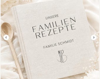 May include: A square, light beige linen-covered recipe book with dark gray text that reads "UNSERE FAMILIEN REZEPTE" and "FAMILIE SCHMIDT" above a simple line drawing of a fork and spoon. A wooden spoon is positioned to the left of the book.