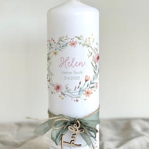 May include: A white pillar candle decorated with a floral wreath and the name "Helen" in pink script. The candle is adorned with a green ribbon, twine, and a wooden charm. The date "5.4.2025" is also printed on the candle.