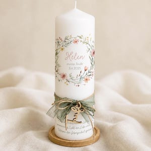 May include: A white pillar candle decorated with a floral wreath and the name "Helen" and date "5.4.2025". The candle is adorned with a green ribbon, wooden charm, and sits on a wooden base. The candle is a decorative item.