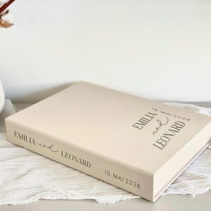 Könnte beinhalten: Eine beige Box mit dem Text "EMILIA and LEONARD 15. MAI 2026" auf der Ober- und Unterseite.