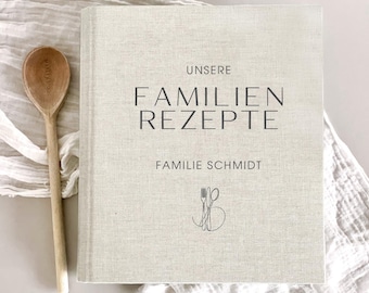 May include: A linen-covered cookbook with the text "UNSERE FAMILIEN REZEPTE" and "FAMILIE SCHMIDT" in black. A wooden spoon with the text "MARLEY COOK" is next to the book. The book has a fork and spoon graphic.