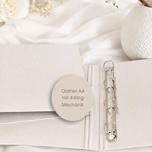 May include: A light beige A4 binder featuring a silver-colored 4-ring metal mechanism. A circular sticker is placed on the cover with the text Ordner A4 mit 4-Ring Mechanik printed in a dark font, indicating the product type and its internal hardware.