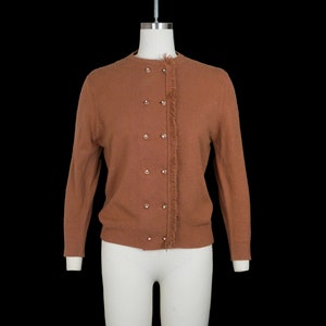 May include: A brown knitted cardigan with a fringe detail on the front and a row of buttons down the front.
