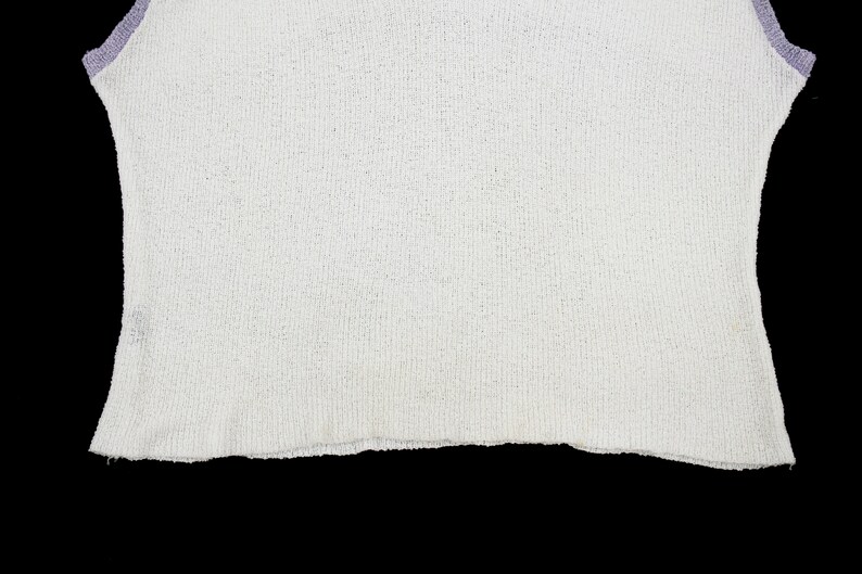 May include: White sleeveless shirt with a purple trim around the neckline and armholes.