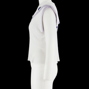 May include: White sleeveless sweater with a purple and blue trim around the neckline. The sweater has a textured knit and a slightly cropped length.