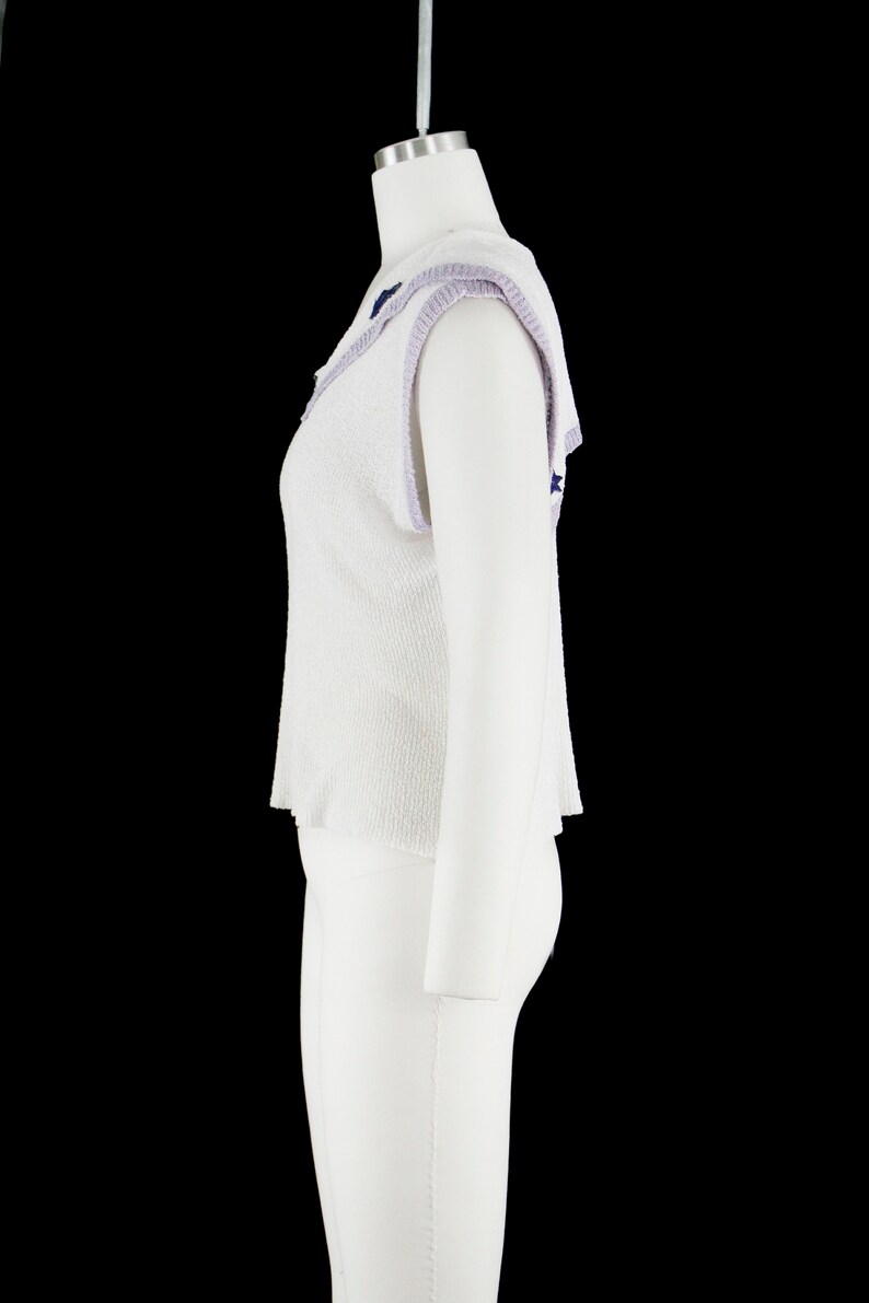May include: White sleeveless sweater with a purple and blue trim around the neckline. The sweater has a textured knit and a slightly cropped length.