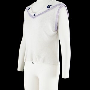 May include: White sleeveless sweater with a lavender trim and navy blue star and anchor embellishments.
