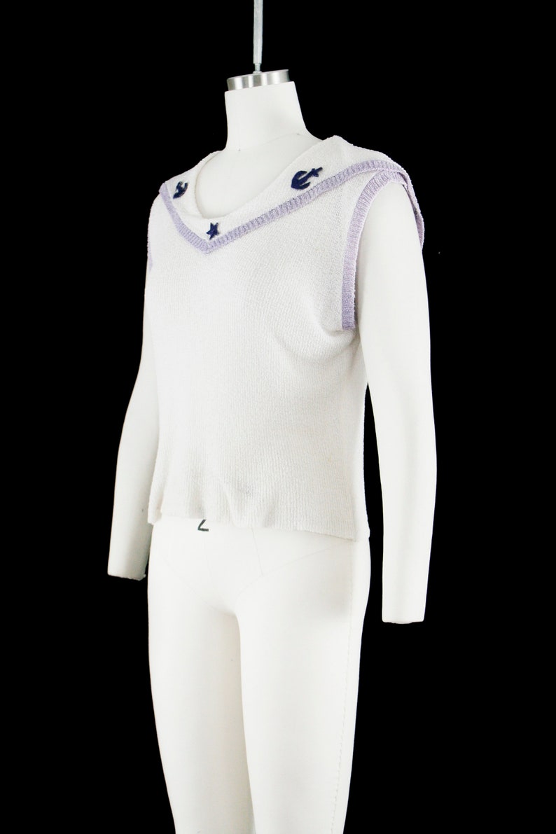 May include: White sleeveless sweater with a lavender trim and navy blue star and anchor embellishments.