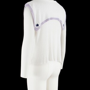 May include: White sleeveless sweater with a lavender trim and blue star accents.
