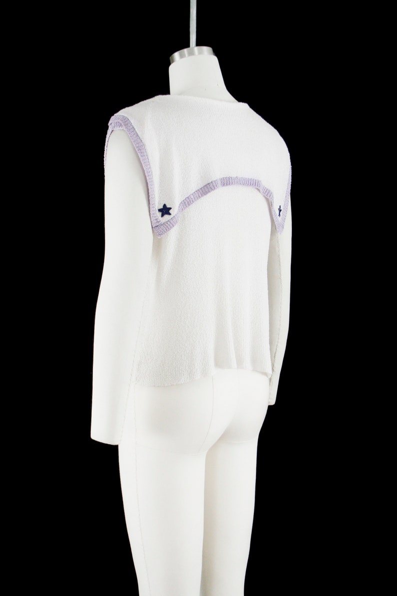 May include: White sleeveless sweater with a lavender trim and blue star accents.
