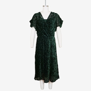 May include: A dark green velvet wrap dress with a short sleeve and a V-neckline. The dress has a textured pattern and a flowing skirt.