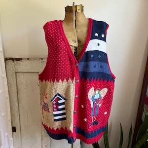 May include: A red, white, and blue knitted vest with a button-up front. The vest features a variety of embroidered designs, including a house, a reindeer, and an angel.