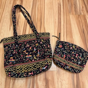 May include: A black tote bag and matching pouch set. The bags feature a colorful floral and bird pattern with red, yellow, and green accents. The tote has two handles and a zipper closure. The pouch has a zipper closure.
