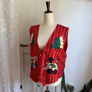 May include: Red vest with gold stripes and Christmas-themed appliqués. The vest features a candy cane, Christmas trees, and a train. The vest has a button-up front and is displayed on a mannequin.