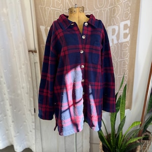 Peut inclure: Une chemise à manches longues boutonnée, à carreaux bleu marine et rouge. La chemise a un col, une poche poitrine et des boutons argentés. Le vêtement est présenté sur un mannequin.