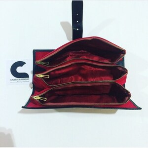 May include: A black leather travel case with three red velvet compartments, each with a gold zipper. The case has a black leather strap with a buckle.
