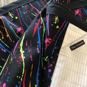 May include: Black fabric with a colorful paint splatter design. The fabric has a black trim and a white label that says "Stay Grounded".