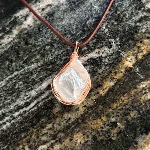 May include: A clear quartz crystal pendant wrapped in copper wire, hanging from a brown leather cord.