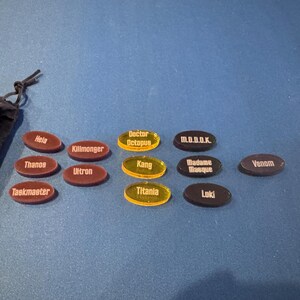Marvel Villainous random tokens displayed in their four sets with a total of 12 villains tokens shown alongside the black velvet bag that they come in.