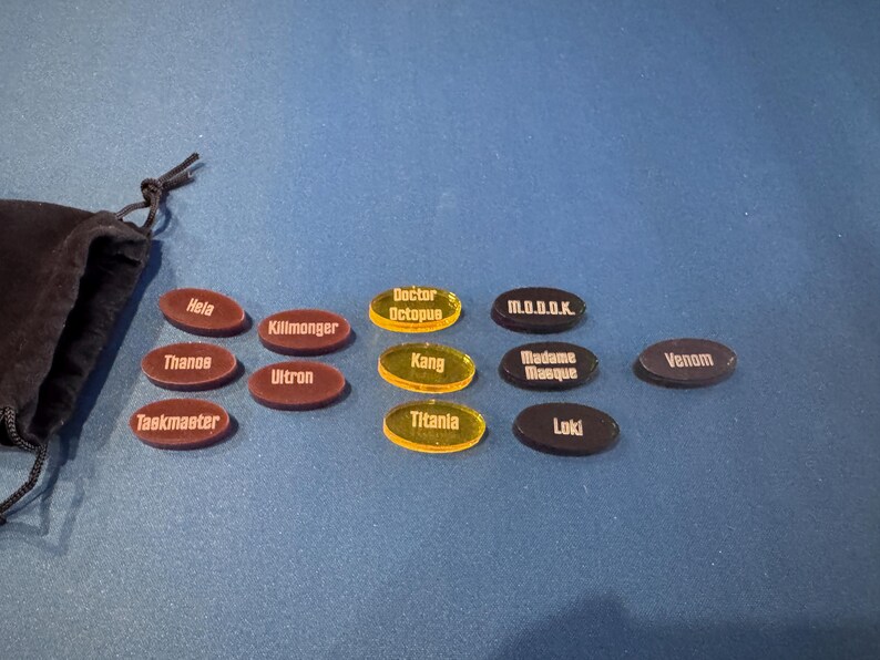 Marvel Villainous random tokens displayed in their four sets with a total of 12 villains tokens shown alongside the black velvet bag that they come in.
