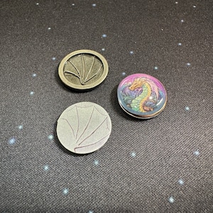 Wyrmspan dragon coins compared to the cardboard coin and metal coin for Wyrmspan. This is the coin sticker set by LaserLand.