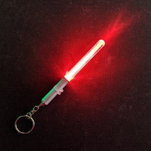 Peut inclure: Un porte-cl&eacute;s argent&eacute; avec une lumi&egrave;re rouge allum&eacute;e. La lumi&egrave;re est de forme cylindrique longue, mince.