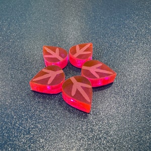 May include: Five pink resin pieces shaped like leaves with white leaf veins arranged in a star shape on a blue surface.