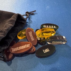 Marvel Villainous random tokens spilling out of the black velvet bag they come in. This set currently includes 12 villain tokens so you can randomize who everyone plays.